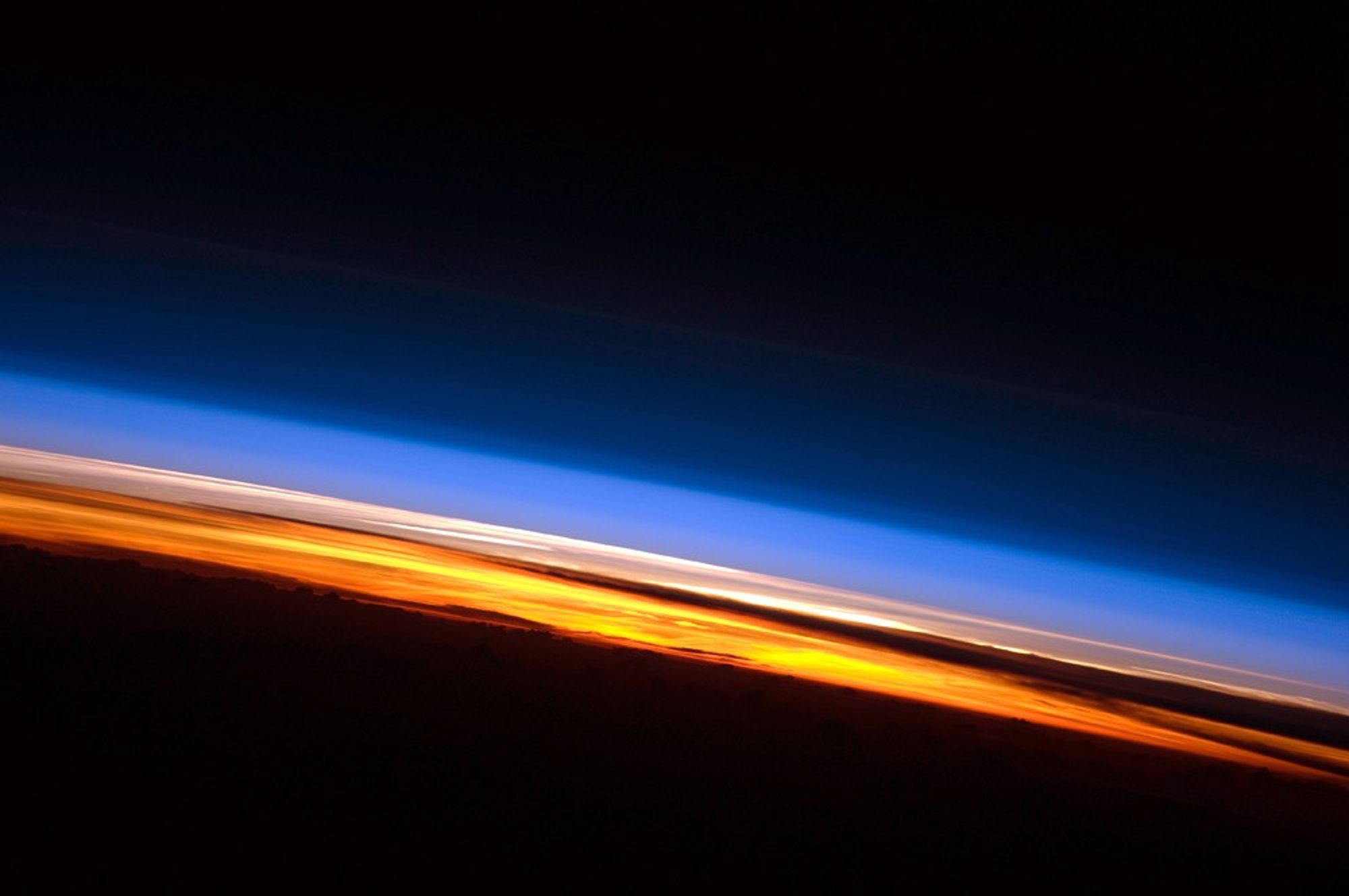 Earth’s blue atmosphere glowing beneath the darkness of space
